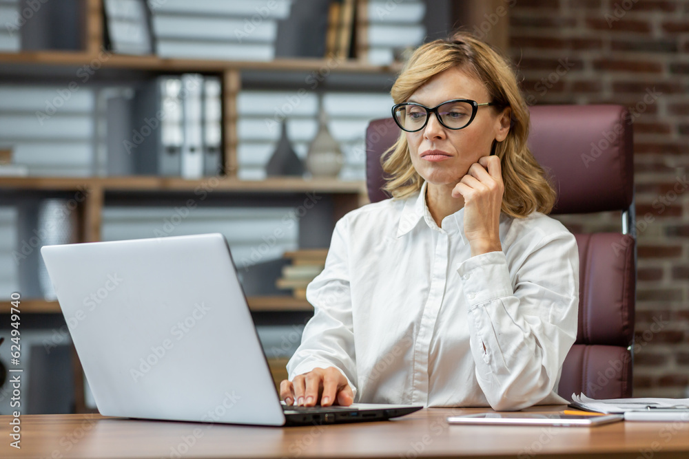Portrait of senior beautiful confident and successful businesswoman, director, boss thinking working at laptop in office. Portrait of senior beautiful confident and successful businesswoman, director, boss thinking working at laptop in office.