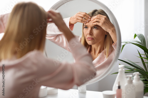 Stressed Mature Lady With Pimple On Forehead Looking In Mirror At Home