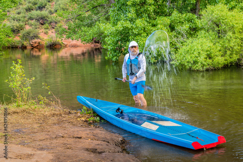 male stand up paddler is splashing and rinsing his paddleboard, Horsetooth Reservoir near Fort Collins, Colorado, in summer scenery
