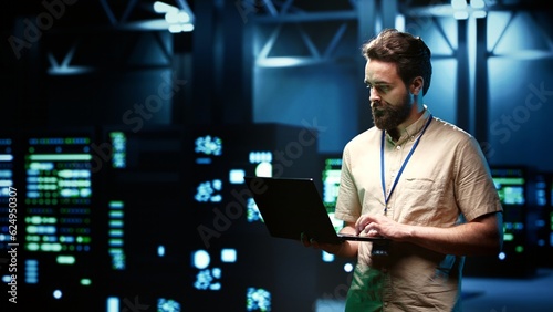 Electrician doing routine system probing, imputing data on tablet of required refurbishing in server rows housing advanced data storage equipment supporting critical IT workloads