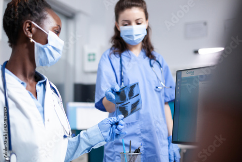 Nurse offering doctor x-ray tomography scan of patient ribcage radiology results. Healthcare specialists wearing antibacterial medical protective workwear in hospital office