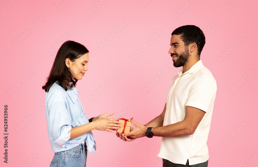 Beautiful young couple exchanging presents, isolated on pink background Beautiful young couple exchanging presents, isolated on pink background