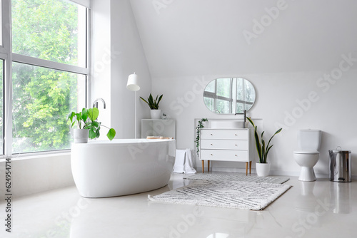 Interior of light bathroom with bathtub, sink on chest of drawers and toilet bowl © Pixel-Shot