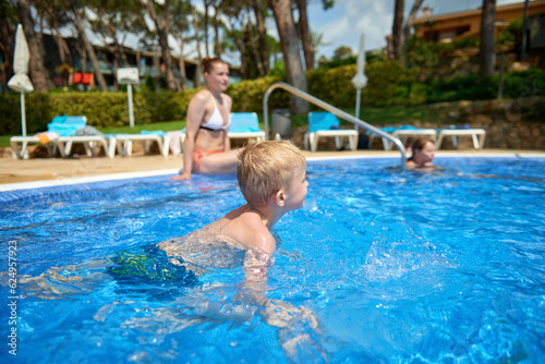 Young boy kid child eight years old splashing in swimming pool having fun leisure activity. Boy happy swimming in a pool. Activities on the pool, children swimming and playing in water, happiness and