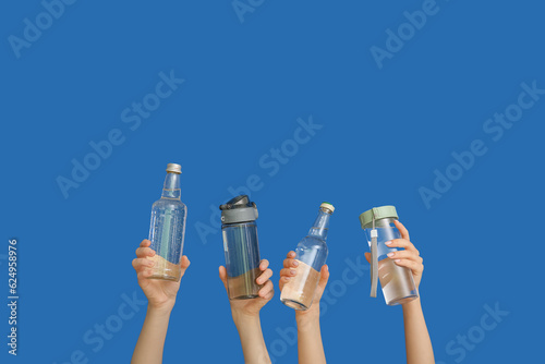 Women holding bottles with clean water on blue background