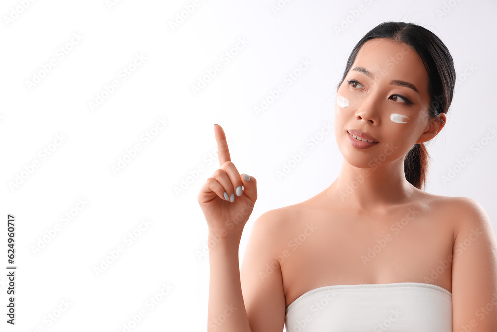 Beautiful Asian woman with cream on her face pointing at something against white background Beautiful Asian woman with cream on her face pointing at something against white background