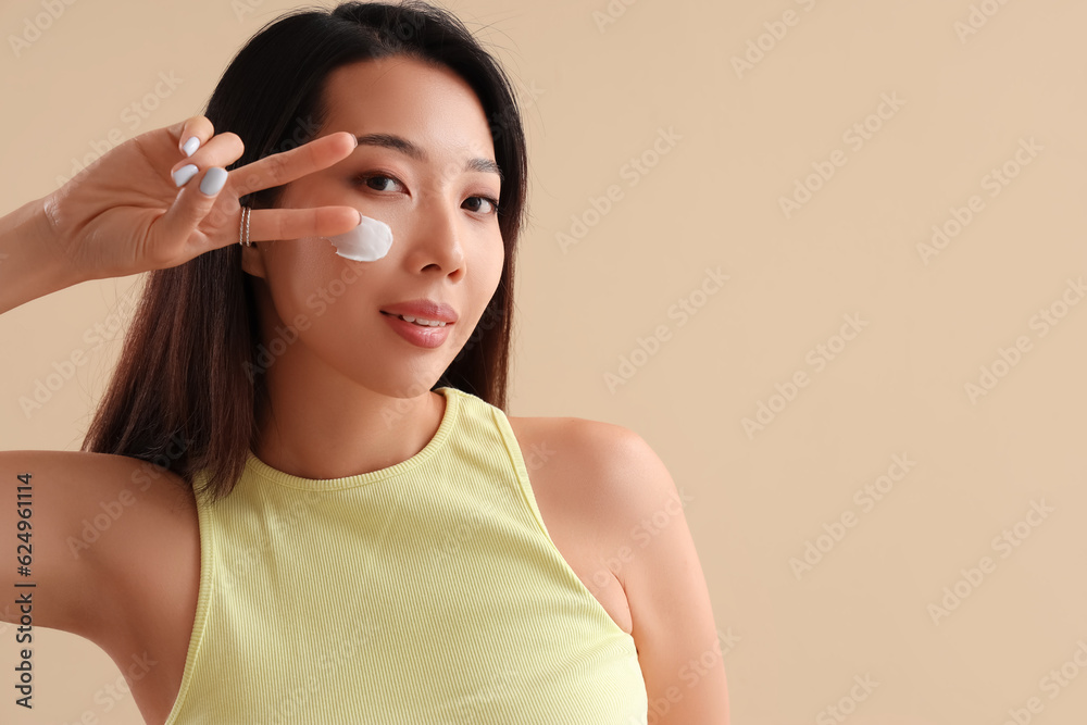 Beautiful Asian woman with cream on her face against beige background Beautiful Asian woman with cream on her face against beige background