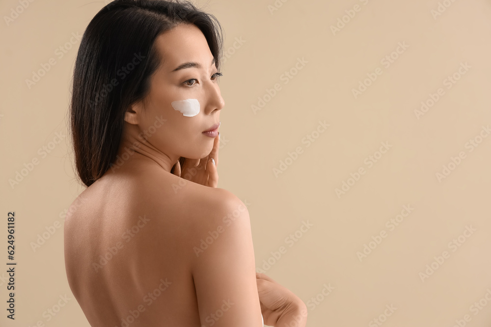 Obraz premium Beautiful Asian woman with cream on her face against beige background
