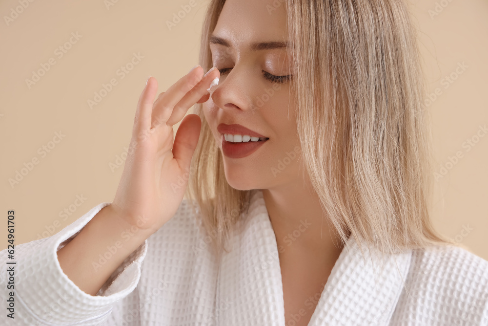 Pretty young woman applying facial cream against beige background Pretty young woman applying facial cream against beige background