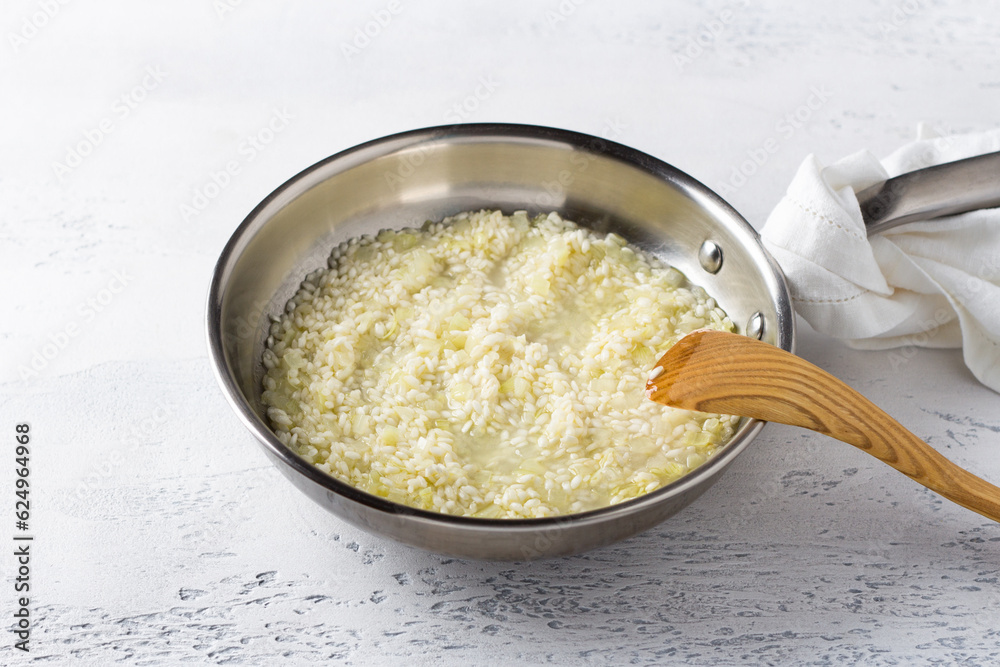 Frying pan with arborio rice, onion and broth on a light blue background. Cooking homemade risotto with pear and gorgonzola, step by step, step 4 Frying pan with arborio rice, onion and broth on a light blue background. Cooking homemade risotto with pear and gorgonzola, step by step, step 4
