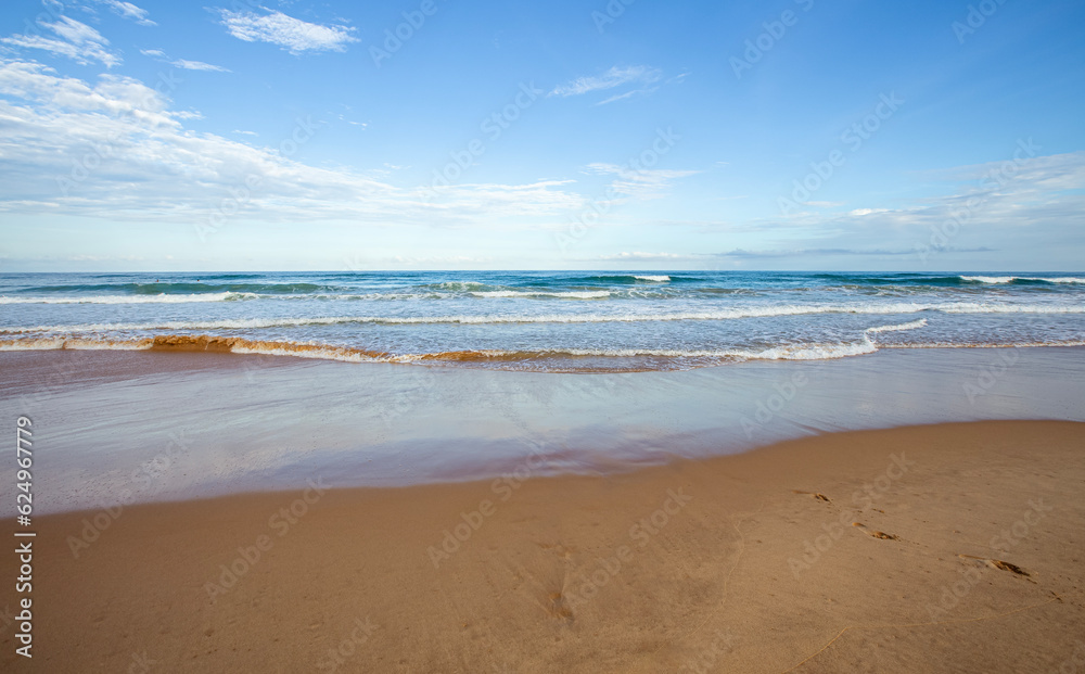 Pegadas na areia da praia deserta em dia ensolarado. Ondas do mar distantes e horizonte do oceano em dia quente com poucas nuvens.