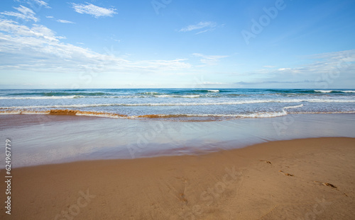 Pegadas na areia da praia deserta em dia ensolarado. Ondas do mar distantes e horizonte do oceano em dia quente com poucas nuvens.