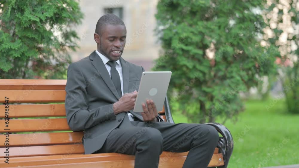 African Businessman Doing Video Chat on Tablet while Sitting Outdoor on a Bench African Businessman Doing Video Chat on Tablet while Sitting Outdoor on a Bench