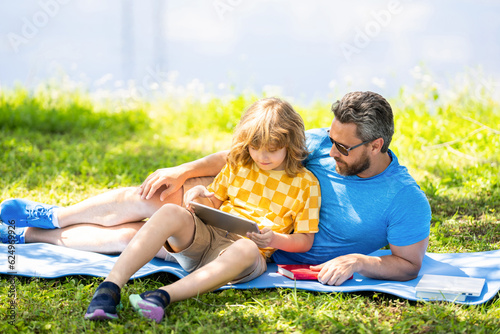 son with father bonding in summer. family education of father and son kid. Father shapes son education with book tablet. Father and son relax in park. childhood school education. quality time reading