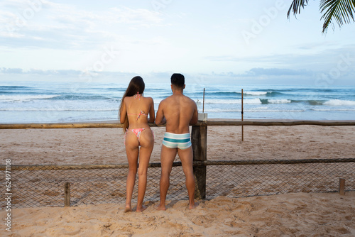 Casal brasileiro usando roupa de banho encostado em mureta de madeira na praia olhando para o mar photo