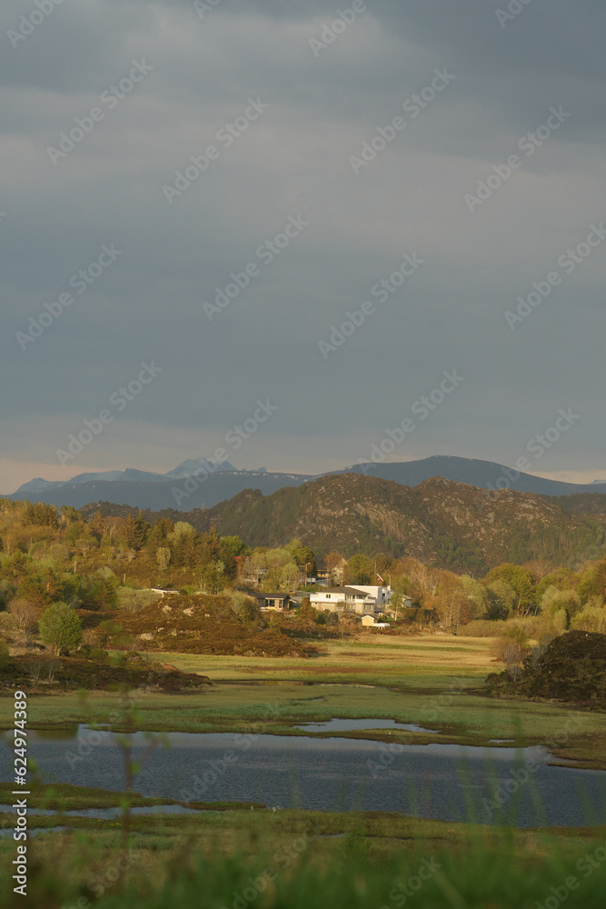 Fototapeta premium View of village in Norway surrounded by mountains at sunset after rain