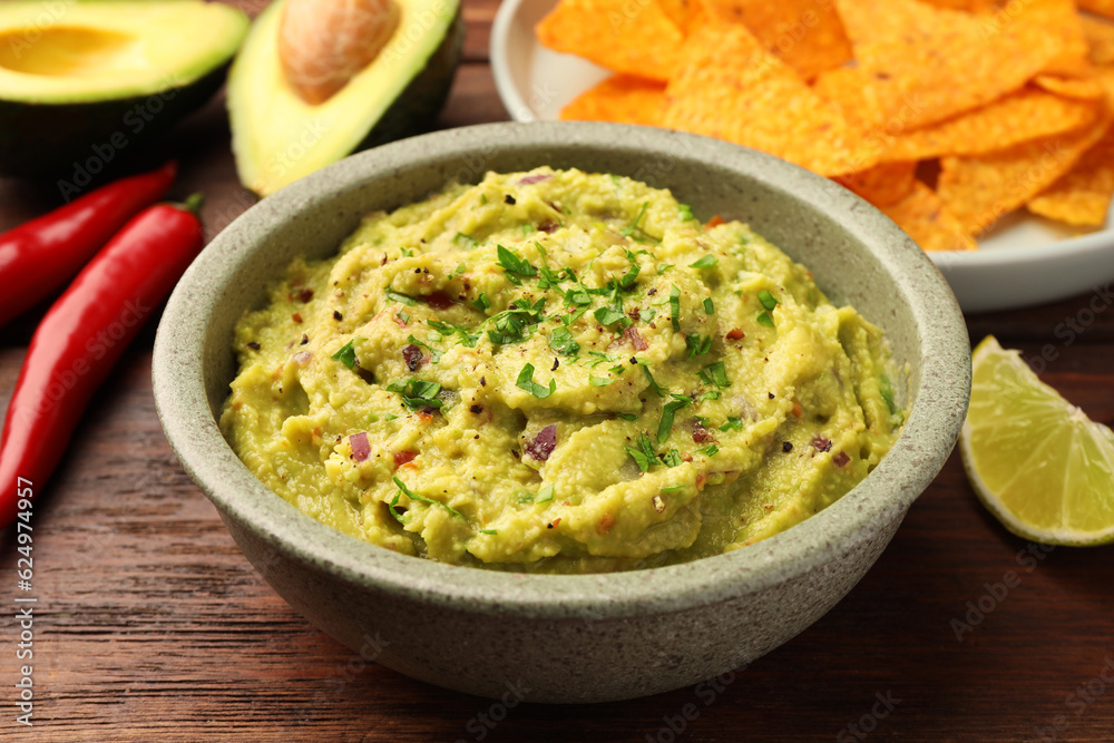 Bowl of delicious guacamole, lime and nachos chips on wooden table, closeup Bowl of delicious guacamole, lime and nachos chips on wooden table, closeup