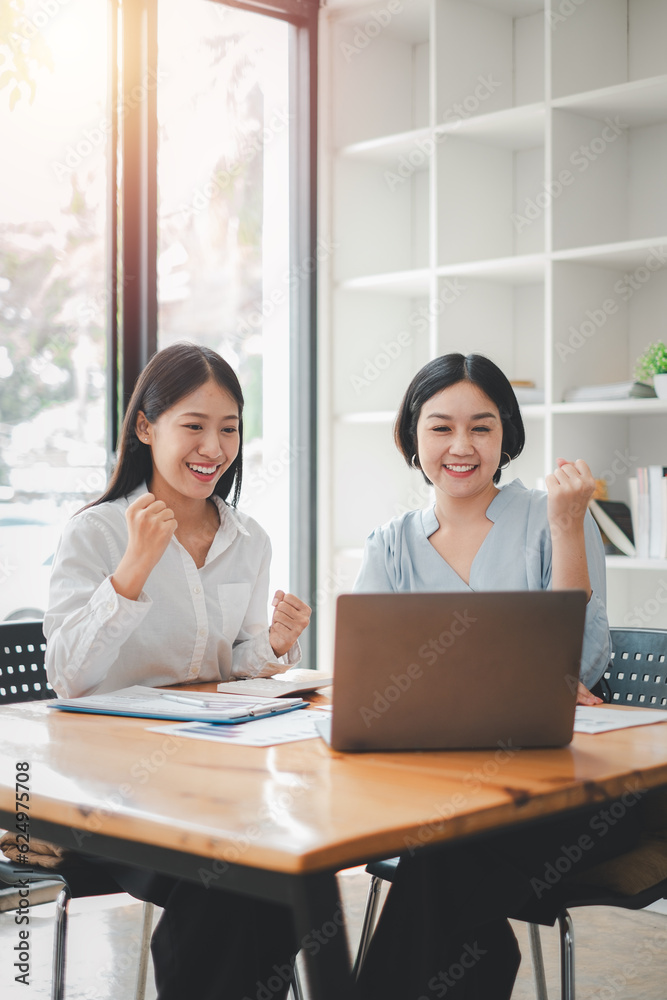 Two businesswomen show joyful expression of success at work smiling happily with a laptop computer in a modern office. Two businesswomen show joyful expression of success at work smiling happily with a laptop computer in a modern office.