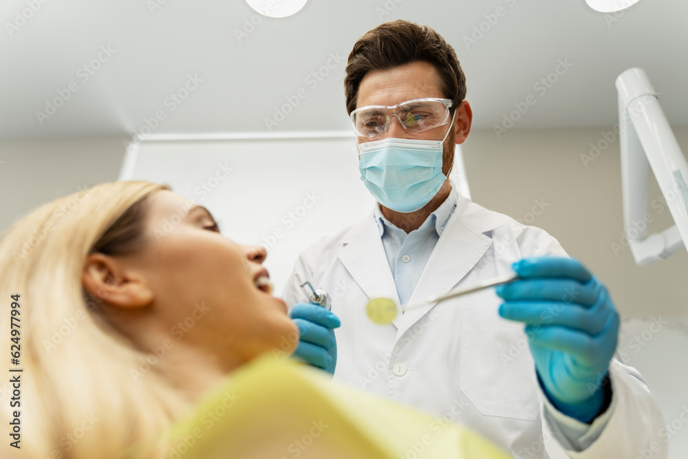 Professional dentist checking quality of teeth. Young beautiful smiling woman, patient sitting in modern dental clinic. Teeth treatment, health care concept