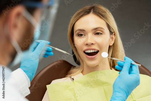 Professional dentist checking quality of teeth. Young beautiful smiling woman, patient sitting in modern dental clinic. Teeth treatment, health care concept