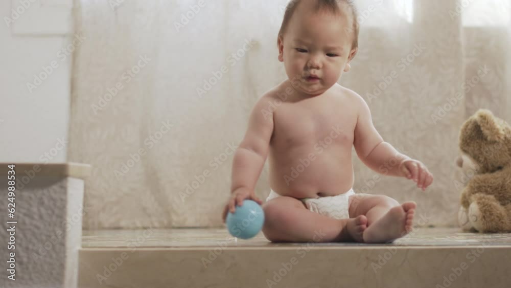 A little asian baby catching and grabbing a ball and throwing it again. Infant learning to gram and pick up things.