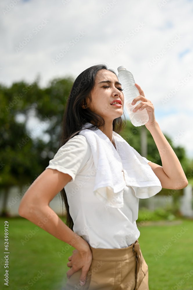 A thirsty and sweaty Asian woman feeling hot and tired after a long run on a sunny day. A thirsty and sweaty Asian woman feeling hot and tired after a long run on a sunny day.