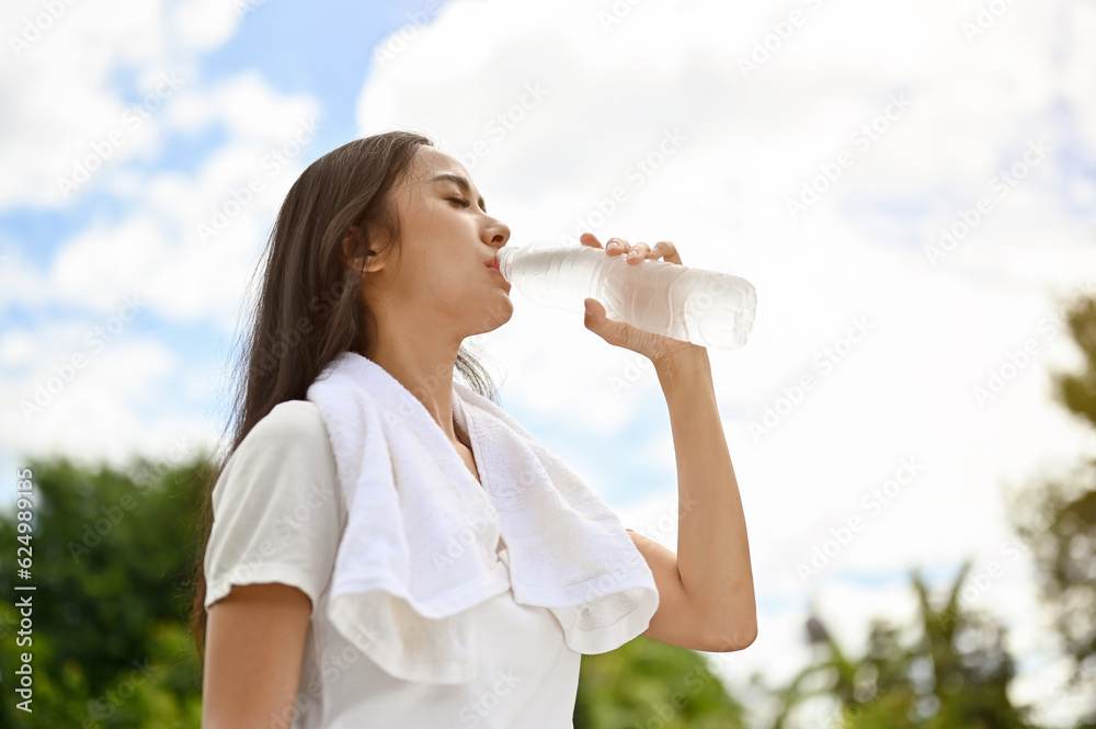 A tired and thirsty young Asian woman is drinking water from a bottle, resting after a long run A tired and thirsty young Asian woman is drinking water from a bottle, resting after a long run