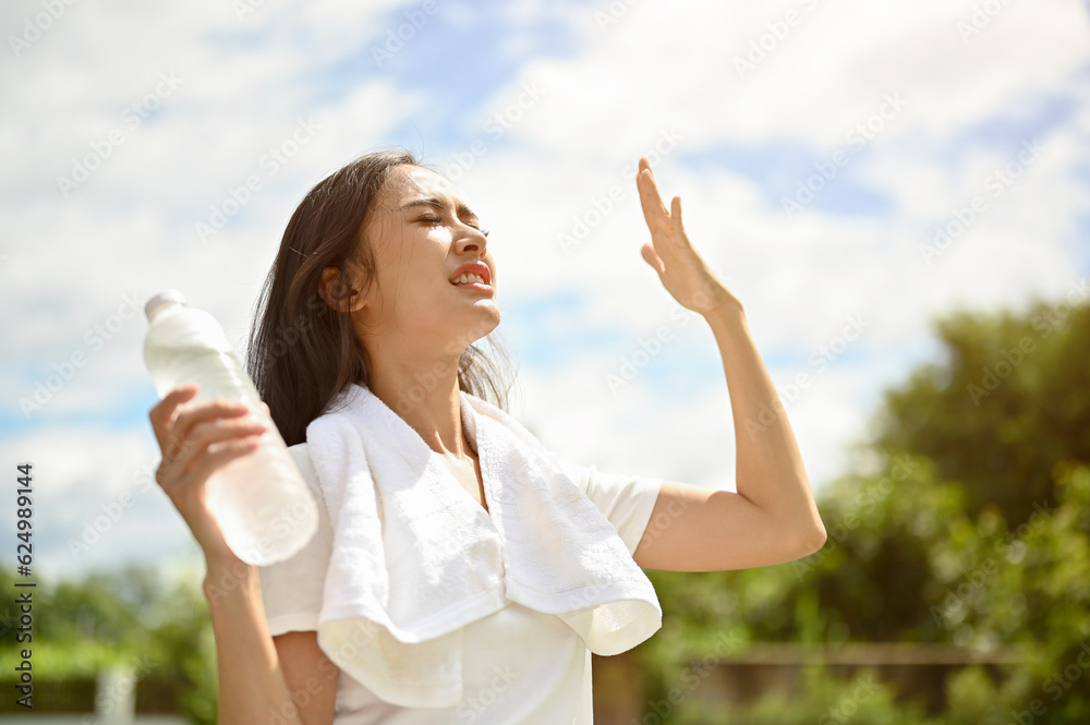 An exhausted Asian woman is fighting the heat wave while running in a park on a sunny summer day An exhausted Asian woman is fighting the heat wave while running in a park on a sunny summer day