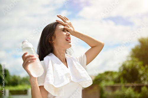 An exhausted Asian woman is fighting the heat wave while running in a park on a sunny day. photo