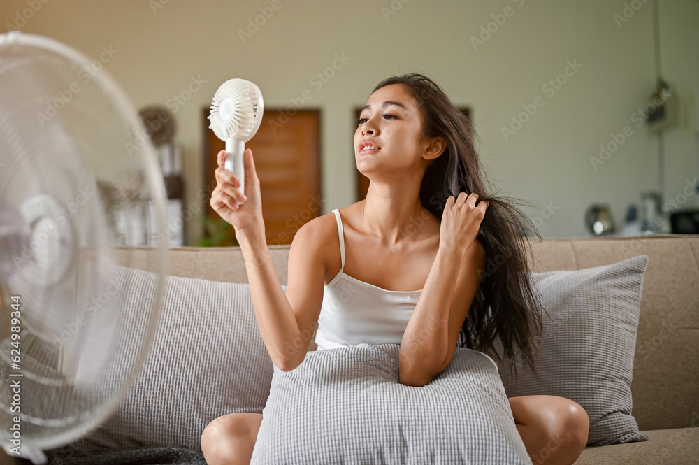 A gorgeous Asian woman, feeling hot and tired, refreshes herself with a handy fan and a a fan A gorgeous Asian woman, feeling hot and tired, refreshes herself with a handy fan and a a fan