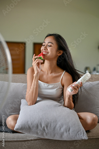A pretty Asian woman enjoys eating fresh watermelon while fighting the heat on a summer day
