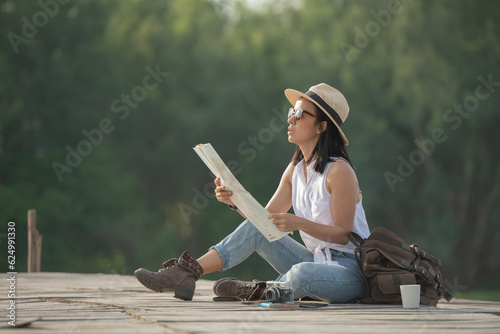 asian woman traveler with map backpack relaxing outdoor with sitting on quayside searching location on map during coffee break on background summer vacations and lifestyle hiking concept.