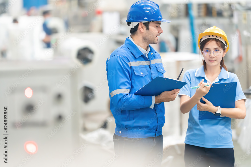 half body photo American engineer and female mechanic foreman in warehouse meeting on mechatronics, holding listnote, walkie talkie, wearing helmet and uniform. In the plastic and steel industry half body photo American engineer and female mechanic foreman in warehouse meeting on mechatronics, holding listnote, walkie talkie, wearing helmet and uniform. In the plastic and steel industry