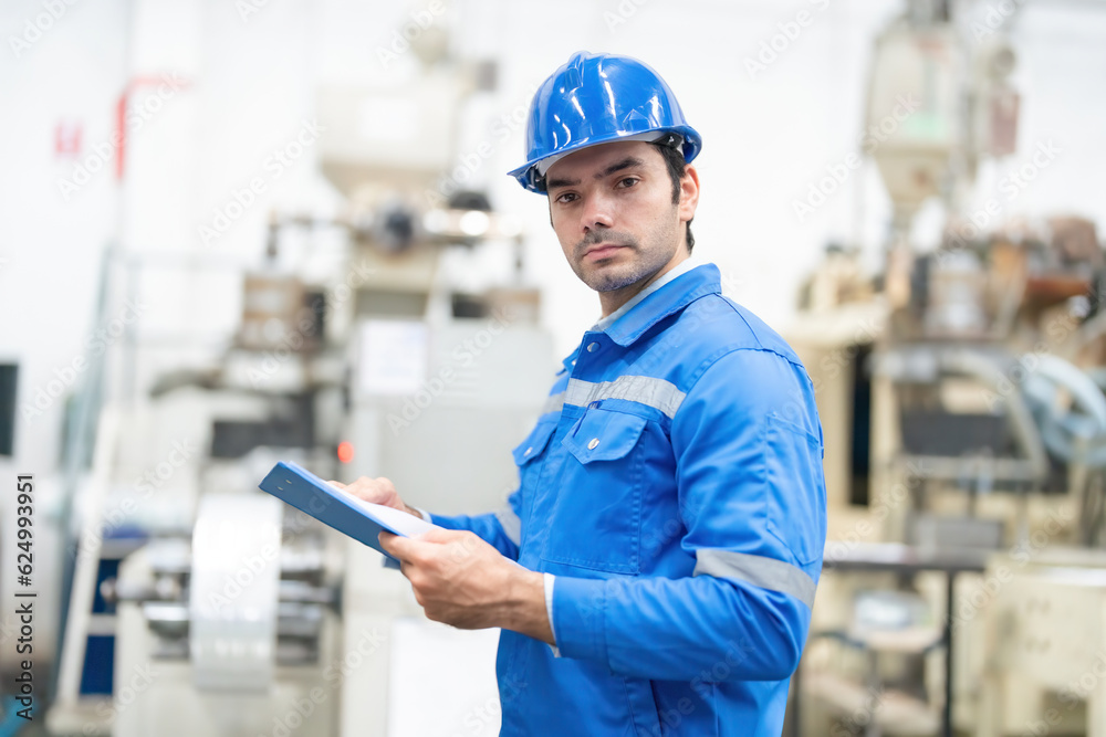 Half body shot of American male engineer, mechanic supervisor Turn sideways and look at the listnote. There are machines working around. Wear a helmet and uniform. In the plastic and steel industry Half body shot of American male engineer, mechanic supervisor Turn sideways and look at the listnote. There are machines working around. Wear a helmet and uniform. In the plastic and steel industry