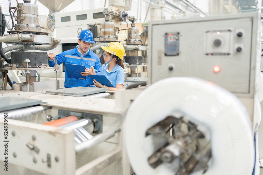 American engineer and female mechanic supervisor Talking to check system of working machinery, holding listnote, walkie-talkie, wearing helmet and uniform, vest, in plastic and steel factory. American engineer and female mechanic supervisor Talking to check system of working machinery, holding listnote, walkie-talkie, wearing helmet and uniform, vest, in plastic and steel factory.