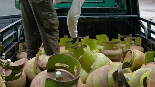 A worker loads liquefied petroleum gas in a green steel metal bottle storage in a truck