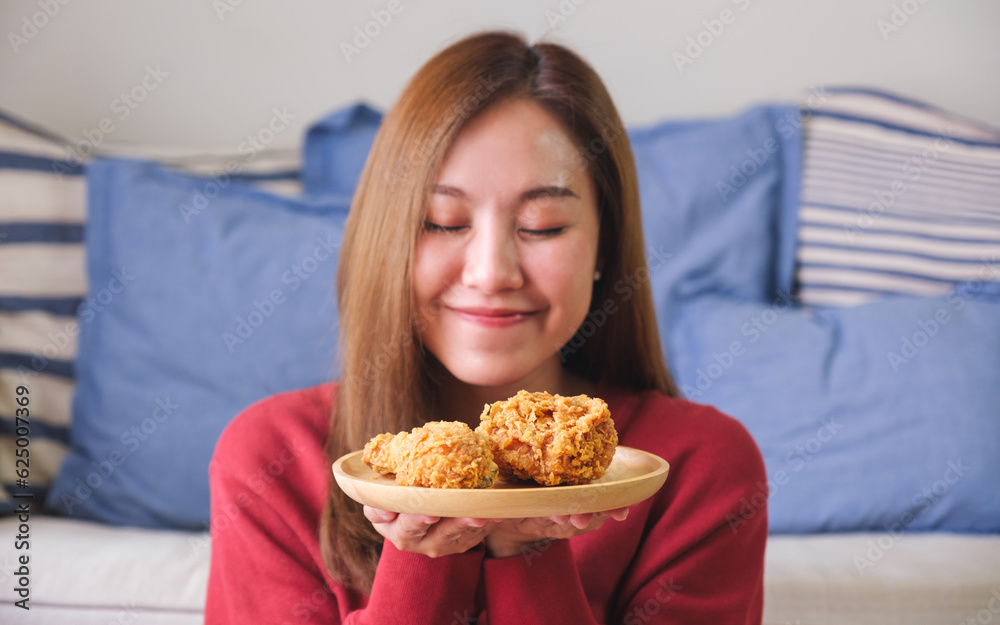 Portrait image of a young woman with closed eyes holding a plate of fried chicken Portrait image of a young woman with closed eyes holding a plate of fried chicken