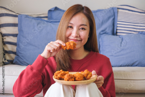 Portrait image of a young woman holding and eating fried chicken at home © Farknot Architect