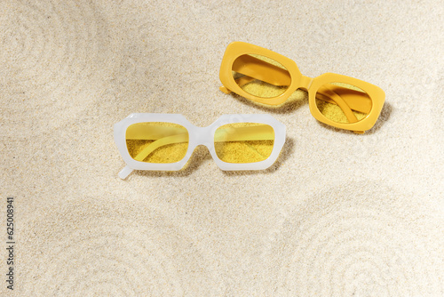 Stylish white and yellow sunglasses on sand background at sunlight, summer fashion collection eyeglasses with colors glass. Summer sale concept. Top view lifestyle aesthetic photo, flat lay