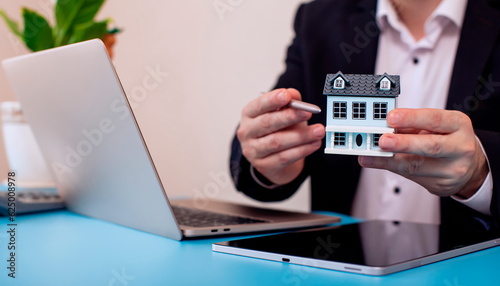 Real estate agent holding house model in front of laptop. Real estate business concept.
