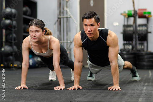 Millennial Asian strong young male and female muscular fitness model athlete couple in sexy sport bra and legging planking bodyweight workout on floor exercise training ready to pushing up in gym