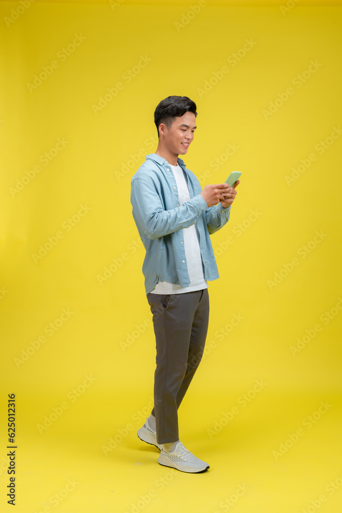 portrait of smiling young casual guy using mobile phone, walking isolated over yellow background portrait of smiling young casual guy using mobile phone, walking isolated over yellow background