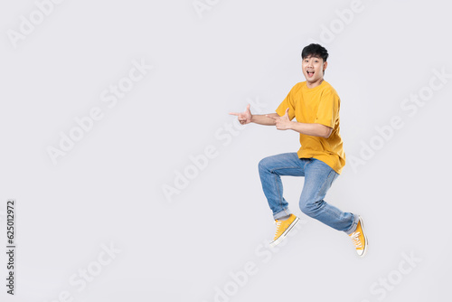 Full length excited handsome young Asian man jumping in air with hand pointing to empty space on white background. Cool man joyful running in copy space. Studio short.