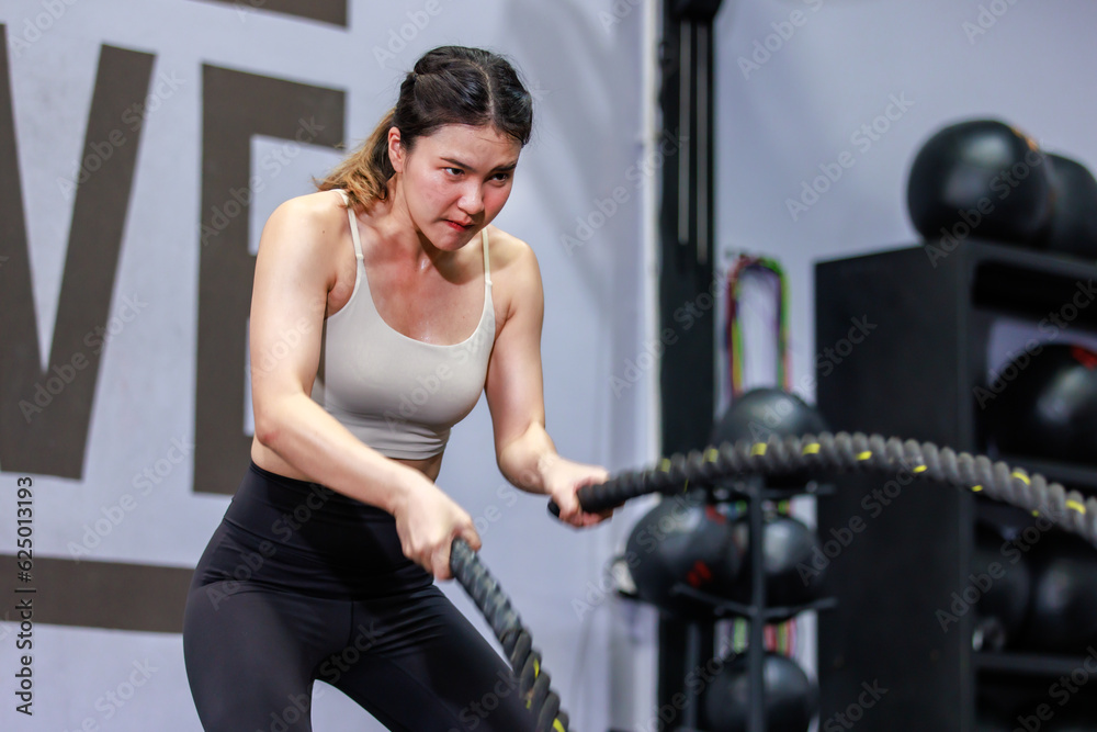 Millennial Asian strong young fit female muscular fitness athlete model in sportswear sexy sport bra and legging standing using stretching heavy rope working out training exercising alone in gym Millennial Asian strong young fit female muscular fitness athlete model in sportswear sexy sport bra and legging standing using stretching heavy rope working out training exercising alone in gym