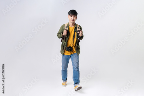 Full length of confident asian man backpacker in a casual outfit, walking with a smile on face on isolated white background. Asian man traveller in studio shot.