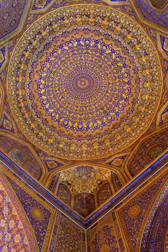Painted gilded dome of Madrasa Tilya Kori  Registan complex . Arabic text of Koran  sacred book of muslims  used as part of ornament. Gold and blue  vertical. Samarkand  Uzbekistan