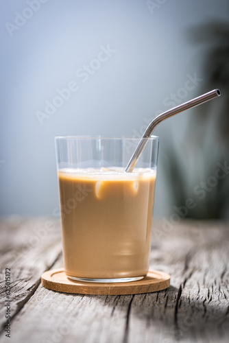 Ice coffee in transparent glass with straw  placed on rustic board. Popular summer coffee cocktail drink.