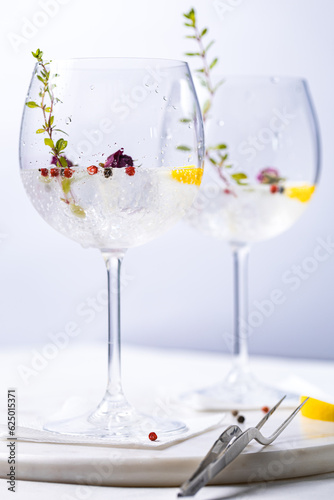 Gin and tonic cocktail with red pepper, lemon and rose buds in gin glasses, in white and bright environment. Perfect summer cocktail drink. 