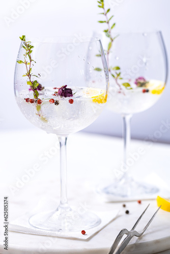 Gin and tonic cocktail with red pepper, lemon and rose buds in gin glasses, in white and bright environment. Perfect summer cocktail drink. 