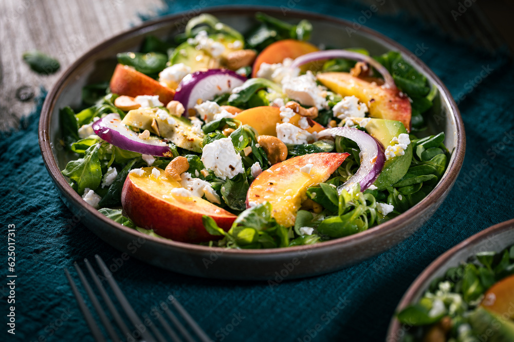 Salad with peach, onion, avocado, nuts and cheese, served on a plate in dark ambient. Healthy super food meal on wooden board. Salad with peach, onion, avocado, nuts and cheese, served on a plate in dark ambient. Healthy super food meal on wooden board.